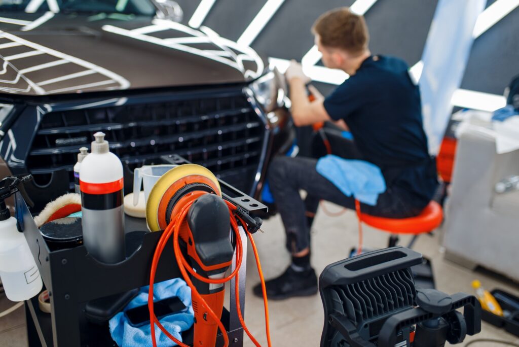 Male worker polishes headlights, car detailing